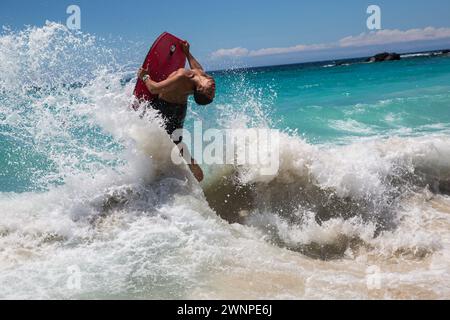 Les habitants chevauchent les vagues sur une plage de sable blanc à Hawaï. Banque D'Images