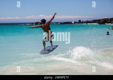 Les habitants chevauchent les vagues sur une plage de sable blanc à Hawaï. Banque D'Images