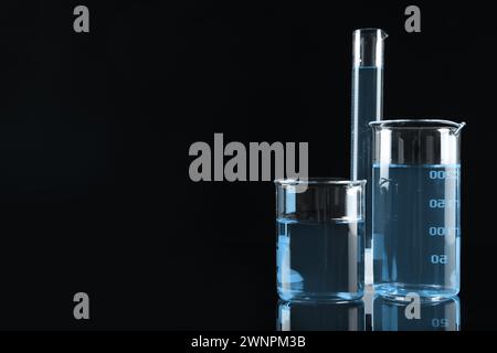 Verrerie de laboratoire avec liquide bleu clair sur fond noir, espace pour le texte Banque D'Images