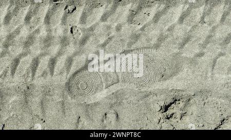 Un imprimé de chaussure sur une piste de pneu sur le sable de plage Banque D'Images