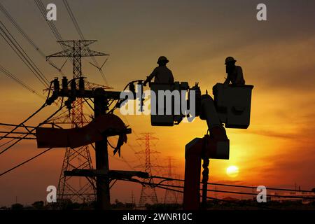 groupe de travailleurs électriques de silhouette travaillant sur la ligne de transmission à haute tension connectée au poteau avec la station de transformateur à haute tension Banque D'Images