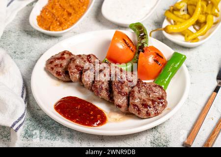 Boulettes de viande grillées. Avec tomates, poivrons, hors-d'œuvre et sauce spéciale. Boulettes de viande turques sur une assiette Banque D'Images