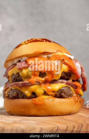 Hamburger double. Avec fromage cheddar, oignons caramélisés, rôti de bœuf et sauce spéciale. Hamburger avec deux boulettes de viande sur la planche de service. Gros plan Banque D'Images