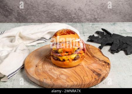 Hamburger double. Avec fromage cheddar, oignons caramélisés, rôti de bœuf et sauce spéciale. Hamburger avec deux boulettes de viande sur la planche de service Banque D'Images