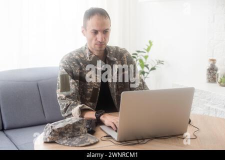 Soldat au bureau. Sérieux jeune homme militaire tapant sur ordinateur portable tout en travaillant dans le bâtiment du quartier général. Un homme caucasien en uniforme de camouflage est assis Banque D'Images