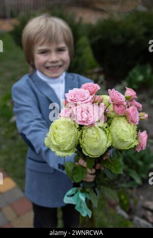 enfant joyeux tient un bouquet de roses roses et vertes devant lui. Fête des mères, Journée internationale de la femme, gratitude, Saint-Valentin. Fleur surp Banque D'Images