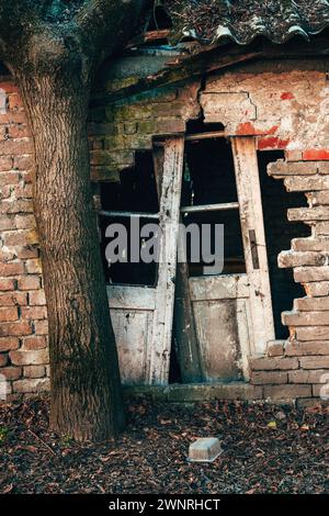 Vieille maison en ruine avec un mur de briques endommagé et des portes cassées prêtes pour l'épuisement, image verticale Banque D'Images