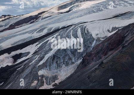 Contraste saisissant de couches de cendres volcaniques sombres et de neige blanche sur une pente de montagne, montrant les textures brutes de la nature et l'histoire dynamique d'un vivant Banque D'Images