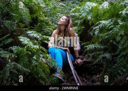 Femme Backpacker et randonneur habillé en bleu assis dans la jungle bronzer sur son visage à la Palma, île des Canaries Banque D'Images