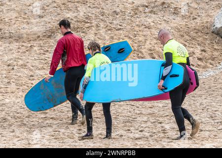 Un moniteur de surf et ses deux apprenants portant leurs planches de surf à Fistral Beach à Newquay en Cornouailles au Royaume-Uni. Banque D'Images