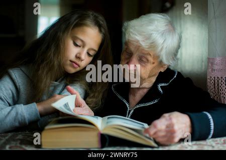 Une grand-mère lit un livre avec sa petite-fille préscolaire. Banque D'Images