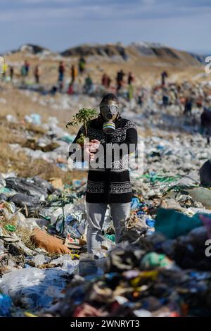 Homme avec masque à gaz et plante sur décharge debout sur décharge, grande pile de déchets, concept environnemental et activisme écologique. Banque D'Images