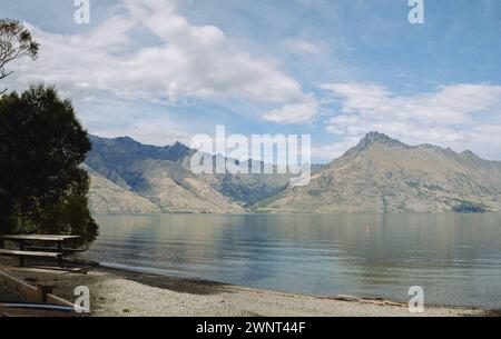 Table de pique-nique sur la plage rocheuse au bord du lac surplombant les montagnes et le ciel Banque D'Images