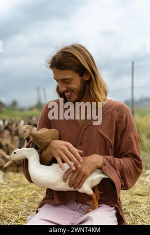 Un homme aux cheveux longs souriant tient des canards dans ses mains. Banque D'Images