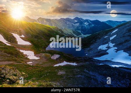 solstice d'été dans les montagnes de roumanie. beau paysage avec le lac capra et la neige sur les collines sous un ciel avec le soleil et la lune. jour et nuit Banque D'Images