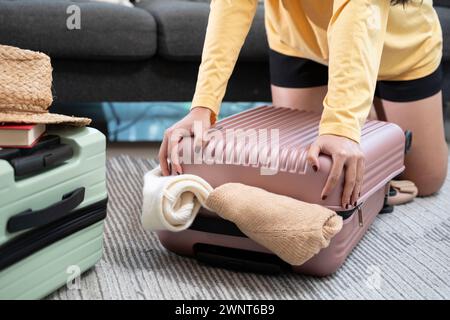 Jeune femme asiatique empilant des vêtements et dans un étui de sac, essayant d'emballer un bagage à main. Banque D'Images