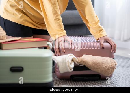 Jeune femme asiatique empilant des vêtements et dans un étui de sac, essayant d'emballer un bagage à main. Banque D'Images