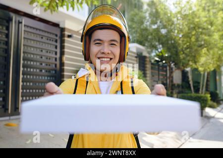 Livreur joyeux en uniforme jaune donnant boîte de pizza fraîche Banque D'Images