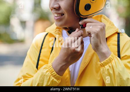 Image recadrée d'un livreur souriant décollant son casque Banque D'Images
