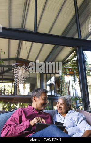 Couple biracial senior profite d'un moment ensemble sur un canapé, entouré de plantes, avec espace de copie Banque D'Images