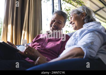 Couple biracial senior aime une tablette ensemble, assis confortablement à l'intérieur Banque D'Images