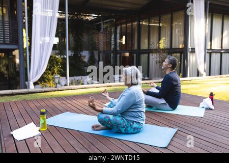 Couple biracial senior pratique le yoga à l'extérieur sur tapis à la maison Banque D'Images