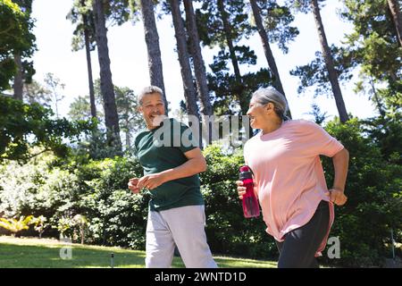 Couple biracial senior aime un jogging dans un parc ensoleillé Banque D'Images