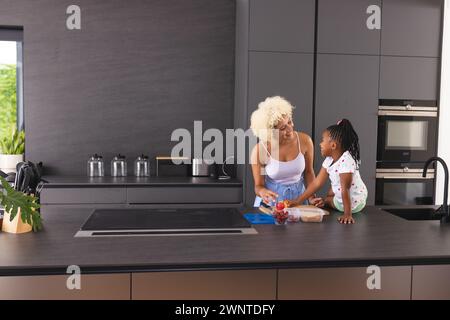 Jeune mère biraciale et fille afro-américaine préparent le déjeuner scolaire dans une cuisine, espace copie Banque D'Images