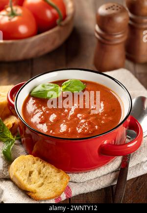 Bol de soupe aux tomates garni de feuilles de basilic et de tranches de baguette grillées sur plateau en bois Banque D'Images