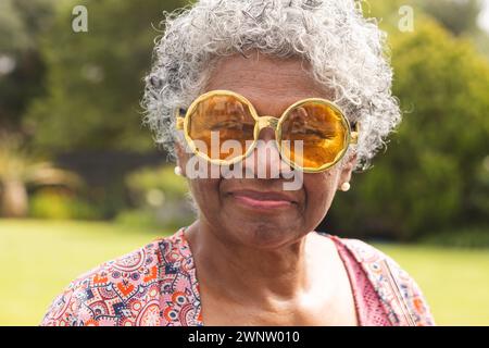 Femme biraciale senior avec les cheveux gris porte de grandes lunettes de soleil ambre et boucles d'oreilles en perles Banque D'Images