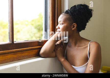 Une jeune femme afro-américaine regarde par une fenêtre, perdue dans ses pensées, avec un espace de copie Banque D'Images