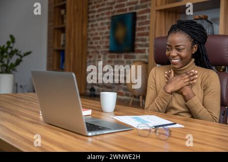 Femme joyeuse avec des dreadlocks à l'aide d'un ordinateur portable s'engage dans l'éducation virtuelle menant des webinaires Banque D'Images