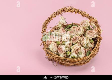 Composition créative avec des roses délicates sèches dans un panier en osier fait maison. Carte de voeux, fond rose pastel, espace de copie Banque D'Images