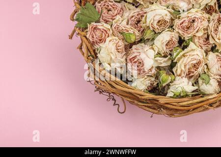 Composition créative avec des roses délicates sèches dans un panier en osier fait maison. Carte de voeux, fond rose pastel, vue de dessus Banque D'Images