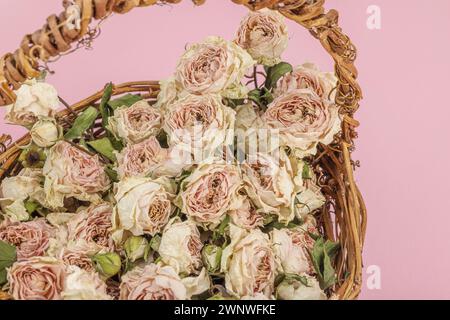 Composition créative avec des roses délicates sèches dans un panier en osier fait maison. Carte de voeux, fond rose pastel, gros plan Banque D'Images