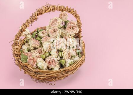 Composition créative avec des roses délicates sèches dans un panier en osier fait maison. Carte de voeux, fond rose pastel, espace de copie Banque D'Images