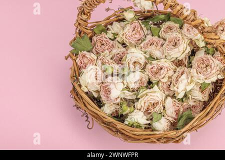 Composition créative avec des roses délicates sèches dans un panier en osier fait maison. Carte de voeux, fond rose pastel, gros plan Banque D'Images