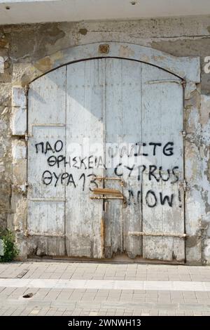 Graffiti politique sur une vieille porte en bois d'atelier. Unissez Chypre maintenant. Larnaca, Chypre. Fév 2024 Banque D'Images