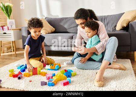 belle mère afro-américaine regardant le téléphone pendant que ses fils jouent avec des cubes à la maison Banque D'Images