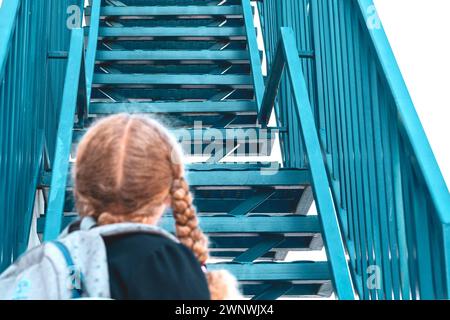 Une écolière regardant les escaliers...Concept école jours, date de début, étape suivante, échelle de carrière, le début de la voie. Fille dans un uniforme avec un bac Banque D'Images