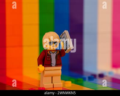 Tambov, Fédération de Russie - 01 octobre 2023 Une figurine Lego Person utilisant un smartphone et debout contre un arc-en-ciel en toile de fond. Banque D'Images