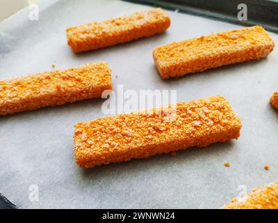 Les bâtonnets de poisson congelés sont disposés sur du papier sulfurisé. Cuisson d'une délicatesse de poisson. Papier cuisson sur une plaque à pâtisserie. Un déjeuner rapide du four. Menu poisson Banque D'Images