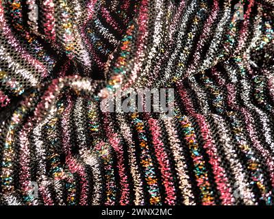 Tissu avec lurex. Textiles tricotés élégants rayés avec des rayures roses, rouges, argentées et dorées sur fond noir. Tissu brûlant, plié négligemment par Banque D'Images