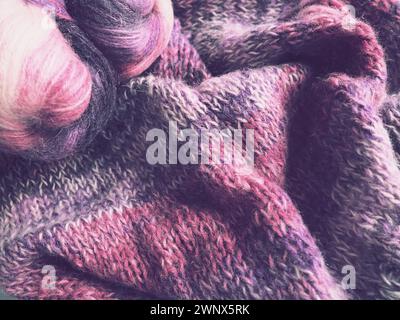 Tricoter une écharpe ou un pull à partir de fil blanc, rose et violet. Boules de laine et de fils acryliques. Tricoter comme passe-temps. Accessoires, aiguilles à tricoter Banque D'Images