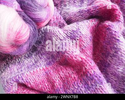 Tricoter une écharpe ou un pull à partir de fil blanc, rose et violet. Boules de laine et de fils acryliques. Tricoter comme passe-temps. Accessoires, aiguilles à tricoter Banque D'Images