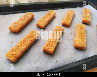 Les bâtonnets de poisson congelés sont disposés sur du papier sulfurisé. Cuisson d'une délicatesse de poisson. Papier cuisson sur une plaque à pâtisserie. Un déjeuner rapide du four. Menu poisson Banque D'Images