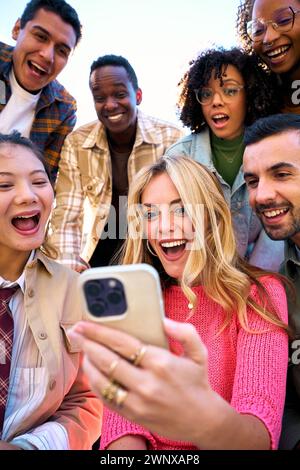 Un groupe d'amis humains heureux étonnés en vêtements d'extérieur en utilisant mobile souriant regardant quelque chose de drôle Banque D'Images