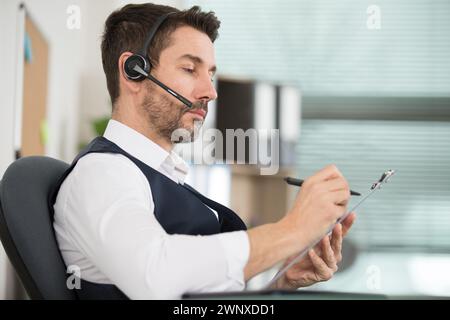 homme au bureau portant un casque et écrivant sur un presse-papiers Banque D'Images