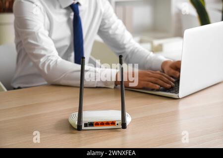 Routeur wi-fi moderne sur la table de l'homme d'affaires utilisant un ordinateur portable dans le bureau, gros plan Banque D'Images