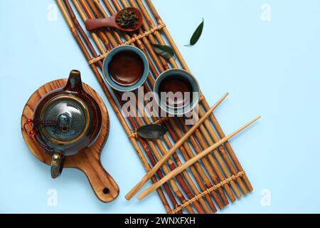 Théière, tasses de thé, cuillère avec des feuilles sèches et des baguettes sur fond bleu Banque D'Images